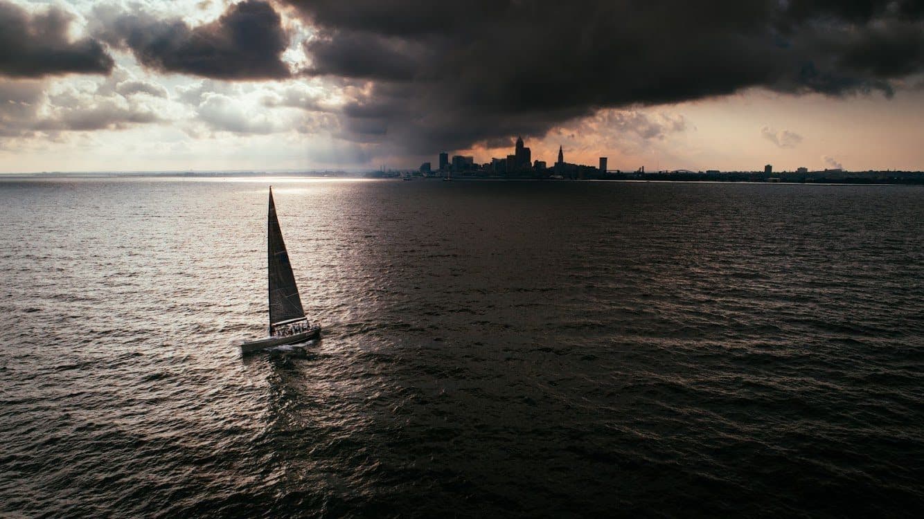 Drone photo of a sailboat on Lake Erie under a storm cloud with the Cleveland skyline behind it