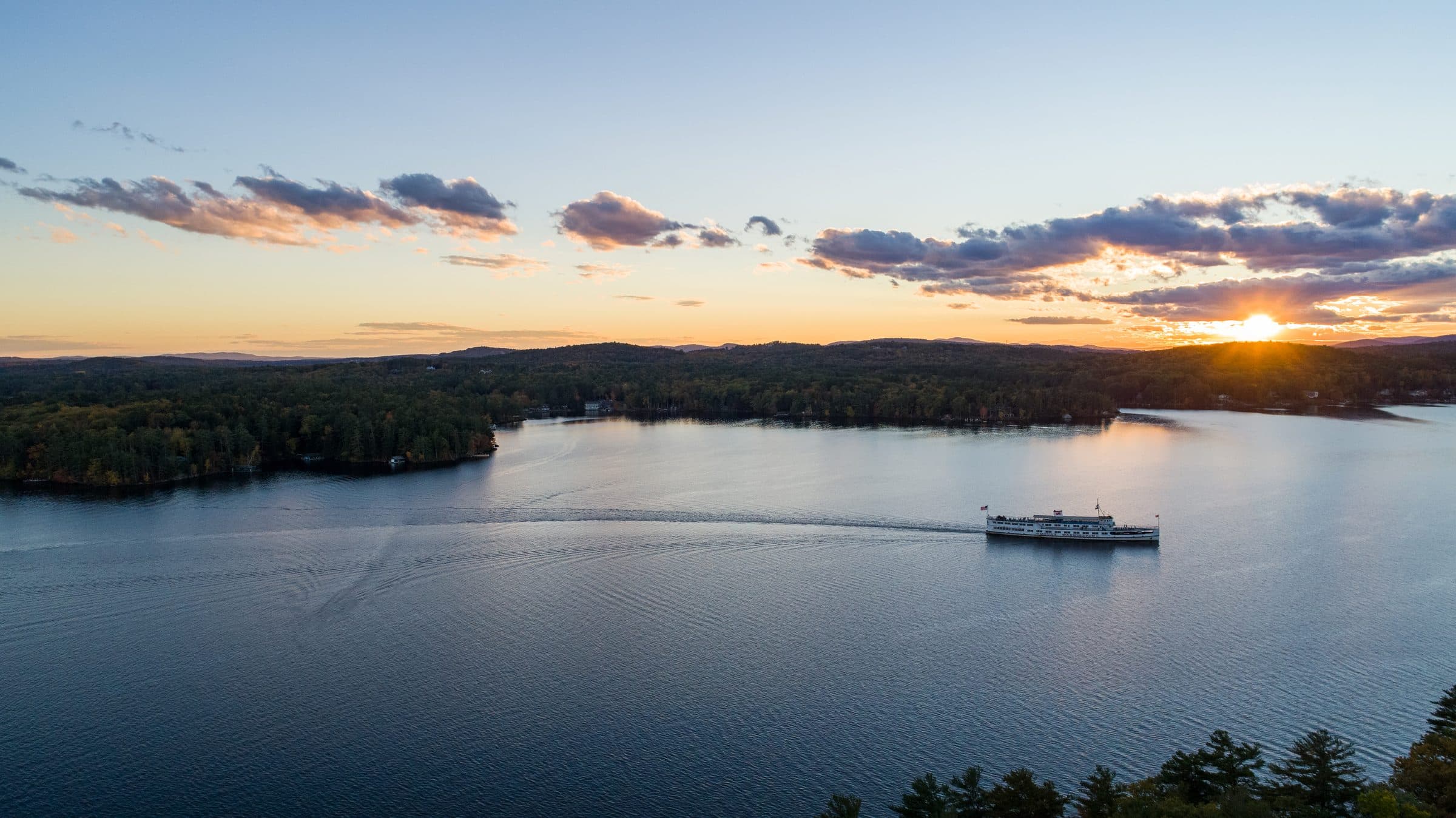 Aerial sunset photo of a passenger cruise boat crossing a calm lake
