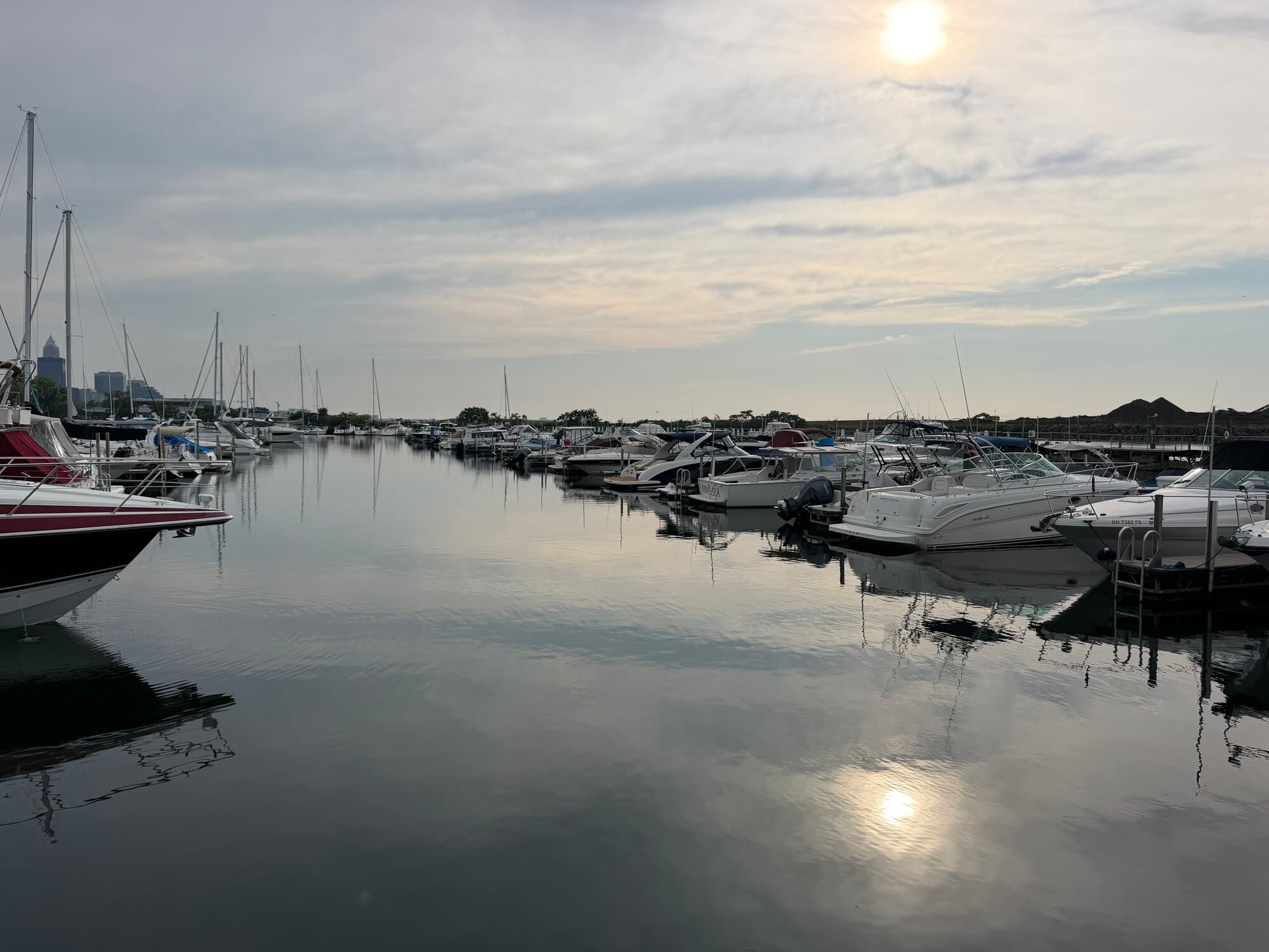 Boats tied in their slips at a calm Cleveland marina on Lake Erie at sunrise, with the downtown skyline in the distance